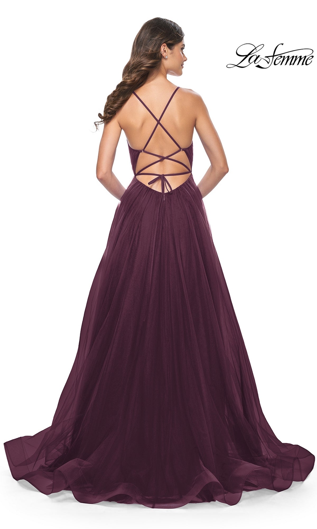 A woman faces away in the La Femme Sheer-Waist Long Prom Ball Gown 31457, featuring a floor-length deep purple a-line silhouette with crisscross straps, open back, and an elegant flowing sheer skirt.